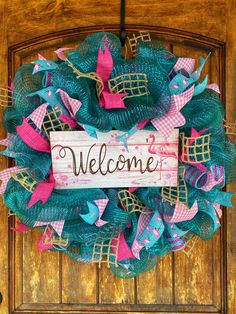 a welcome sign is attached to a wreath on the front door with pink and blue ribbons