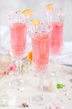 two champagne flutes filled with pink liquid and topped with lemon wedges