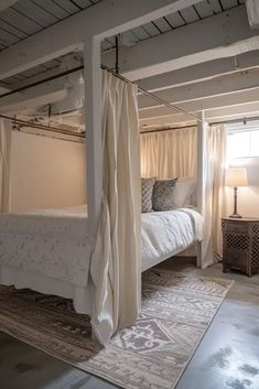 a white bed sitting in a bedroom next to a window with curtains on top of it