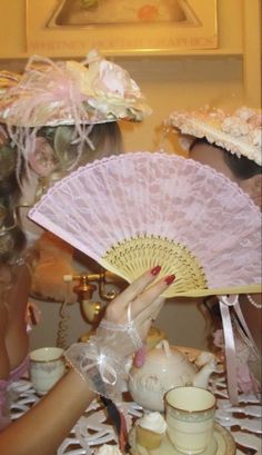 a woman holding a pink fan over a tea set