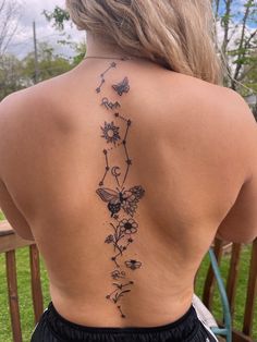 the back of a woman's tattoo with flowers and butterflies on her lower back