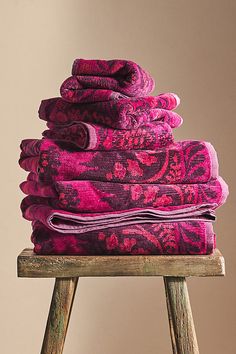 a stack of pink towels sitting on top of a wooden stool next to a wall