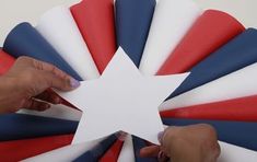 two hands are holding a piece of paper that is shaped like a star and has red, white, and blue strips on it