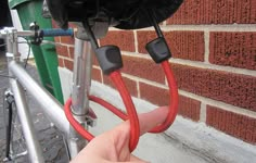 a hand holding a red hose connected to a bike handlebar on the side of a brick building