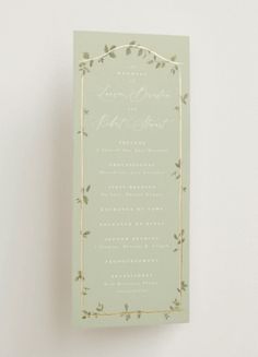 a green wedding card with gold foil on the front and back, sitting on top of a white wall