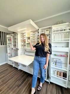 a woman standing in front of a white desk and shelving with lots of shelves