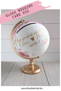 a white globe with gold lettering on it and a pink ribbon around the top that says,