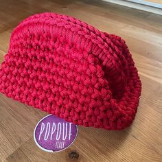 a red crocheted hat sitting on top of a wooden floor next to a sticker