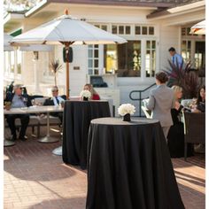 an outdoor dining area with black table cloths and white flowers in vases on round tables