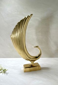 a gold sculpture sitting on top of a white table next to a flower vase with flowers in it