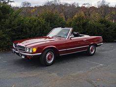 a red convertible car parked in a parking lot next to some bushes and shrubbery