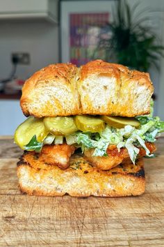 a chicken sandwich with lettuce and pickles on a cutting board