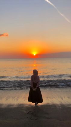 a woman standing on the beach at sunset