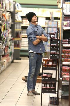 a man standing in the aisle of a grocery store with his arms crossed and looking up