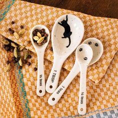 three white measuring spoons with black cat design on them and dog food in the bowl