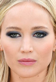 a close up of a woman with blue eyeshadow and blonde hair wearing gold hoop earrings