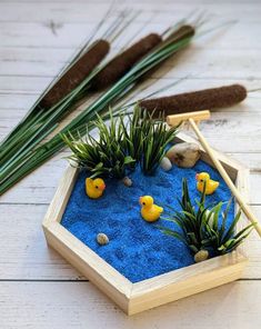 a wooden tray with plants and rubber ducks in it on a white wood floor next to some fake grass