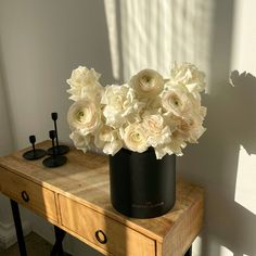 a black vase filled with white flowers on top of a wooden table