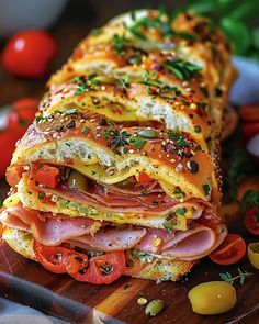 a ham and cheese sandwich cut in half on a cutting board with tomatoes, olives, and herbs