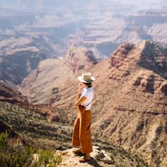 a woman standing at the edge of a cliff looking out into the grand canyon with mountains in the background