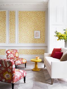 two chairs and a table in a room with yellow flowers on the wall behind them