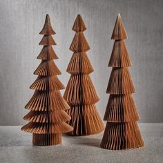 three wooden christmas trees made out of folded paper, on a table with grey background