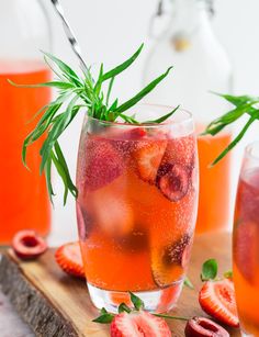 two glasses filled with liquid and strawberries on top of a cutting board next to bottles