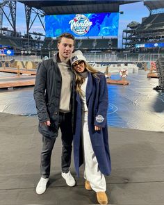 a man and woman posing for a photo in front of a large screen at a stadium