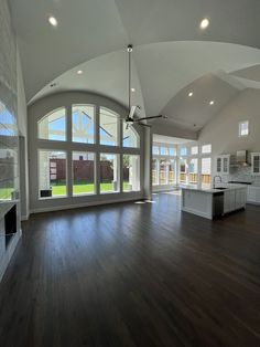 an empty living room with large windows and wood flooring in front of the kitchen