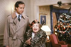 an older woman standing next to a man in front of a christmas tree