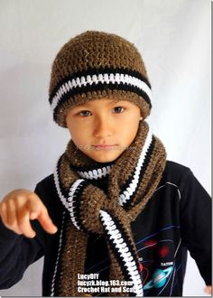 a young boy wearing a knitted hat and scarf, pointing at the camera with his finger