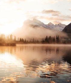 the sun is setting over a lake with mountains in the background and clouds reflecting on the water