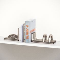 two books are sitting on top of a book shelf next to a pair of metal pipes