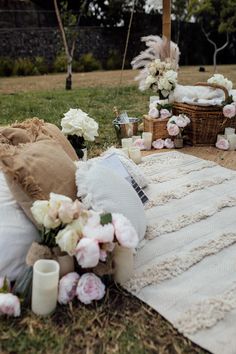 a blanket, pillows and candles on the ground in front of some baskets with flowers