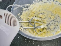 a mixing bowl filled with yellow batter on top of a black counter next to an electric mixer