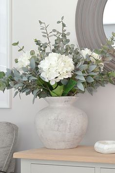 a white vase filled with flowers sitting on top of a table next to a mirror