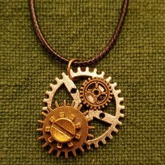 a necklace with two gears attached to it on a green cloth covered surface, one is gold and the other is silver