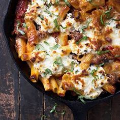 a skillet filled with pasta and cheese on top of a wooden table next to a fork