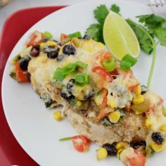 a white plate topped with an enchilada covered in black beans and corn