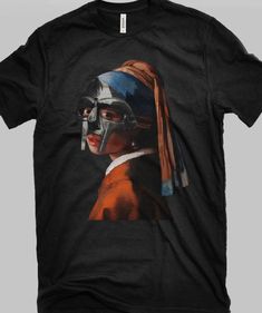 MF Doom x  T-Shirt. The image is printed near the center chest region.  We use high quality unisex pre-shrunk cotton tees.  This shirt is printed using an industry standard printer with DTG (direct to garment) method.  Wholesale & Bulk discounts available - MESSAGE US Shipping Time: We ship out 3-5 business days after payment has been received (we have expedited 1-2 day shipping as an option also) *Wash in cold water and garment inside out for best durability and results. Dry on low temperature Black T-shirt With Sublimation Print In Ring-spun Cotton, Unisex Graphic Tee For Fan Merchandise, Fan Merchandise Graphic Print T-shirt In Ring-spun Cotton, Unisex Custom Print T-shirt For Fan Merchandise, Unisex Custom Print T-shirt For Fans, Custom Print Fan Merchandise T-shirt, Unisex Pop Culture T-shirt With Sublimation Print, Unisex Black T-shirt In Ring-spun Cotton, Graphic Tee With Sublimation Print In Ring-spun Cotton