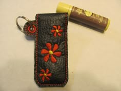 a leather keychain with red flowers on it next to an orange lip bale