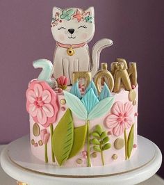 a decorated cake with a cat and flowers on it's top, sitting on a table