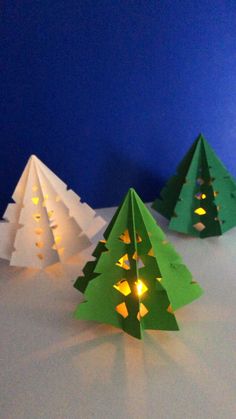 three paper christmas trees sitting on top of a white table next to a blue wall