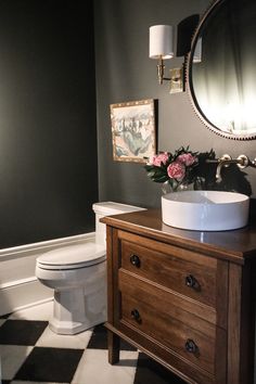 a white toilet sitting next to a bathroom sink under a mirror on top of a wooden cabinet