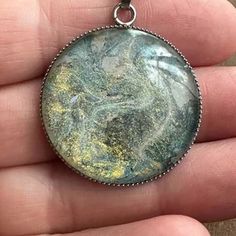 a person is holding a pendant with green and yellow paint on it's surface