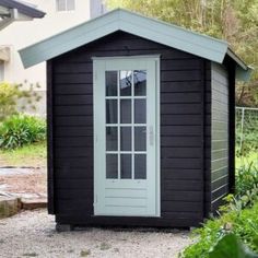 a small black shed sitting in the middle of a garden