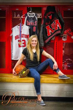 a woman sitting on a bench in front of a locker with baseballs and jerseys