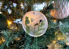 an ornament hanging from a christmas tree with green leaves and flowers on it