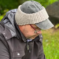 a man wearing a hat and glasses is looking at his cell phone while sitting in the grass