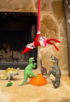 three toy dinosaurs are playing in front of a fireplace with an elf on it's head